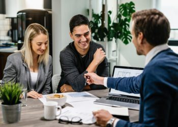 Happy couple having a meeting with real estate agent and analyzing blueprints while communicating.