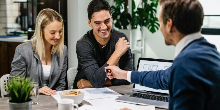Happy couple having a meeting with real estate agent and analyzing blueprints while communicating.