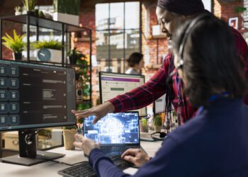 Call center onboarding specialist training new agent on helpful artificial intelligence tools. African american manager in customer support department office shows man how to use company AI software
