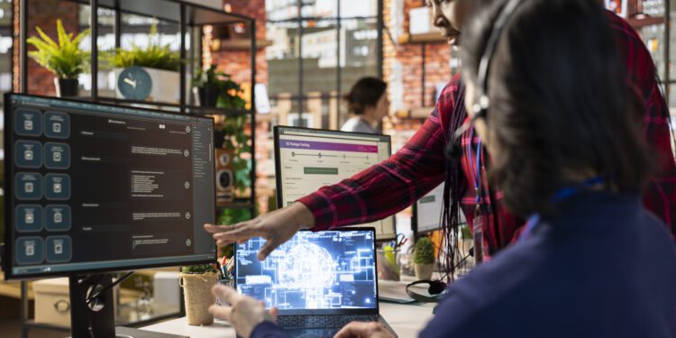 Call center onboarding specialist training new agent on helpful artificial intelligence tools. African american manager in customer support department office shows man how to use company AI software