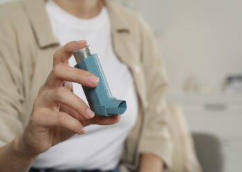 Woman holding asthma inhaler indoors, closeup. Space for text