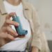 Woman holding asthma inhaler indoors, closeup. Space for text
