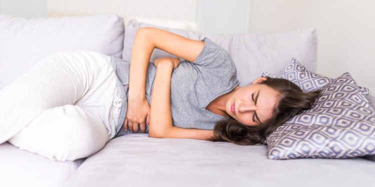 Women have abdominal pain because of menstruation lying in couch and holding her stomach.