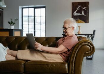 Senior woman sitting on a leather couch using a laptop.
