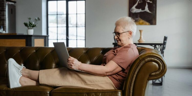 Senior woman sitting on a leather couch using a laptop.