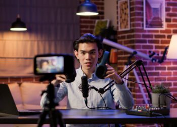 Asian influencer filming headphones review on podcast episode, recording recommendation video on camera. Live broadcasting talk show with wireless headset product on social media.
