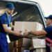 Delivery men loading carboard boxes in a van while getting ready for the shipment.