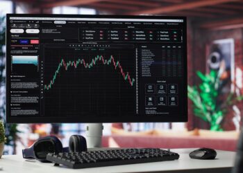 Empty workspace desktop running day trading stock market trends in stylish apartment. PC used for monitoring investment numbers and candle stick charts, a comfortable environment.