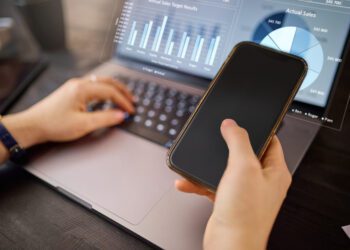 Hands, phone and laptop with hologram in analytics for chart, graph or marketing statistics. Hand of analyst checking 3D digital data for corporate or company sales on computer with smartphone mockup.