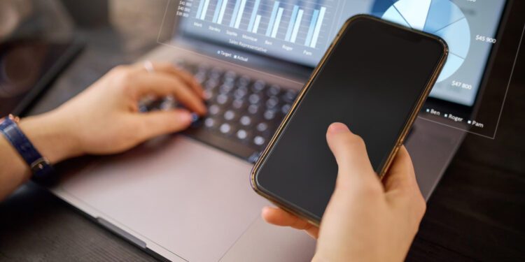 Hands, phone and laptop with hologram in analytics for chart, graph or marketing statistics. Hand of analyst checking 3D digital data for corporate or company sales on computer with smartphone mockup.
