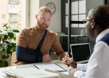 Portrait of man with hand in sling talking to insurance broker after workplace injury or accident