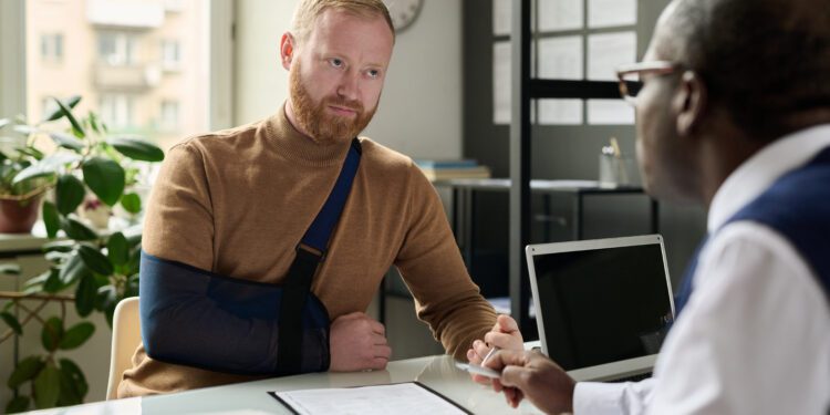 Portrait of man with hand in sling talking to insurance broker after workplace injury or accident
