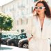 Portrait of young sexy modern businesswoman model. Hot beautiful woman in white suit posing on the street background. Fashion female walking outdoors in sunglasses