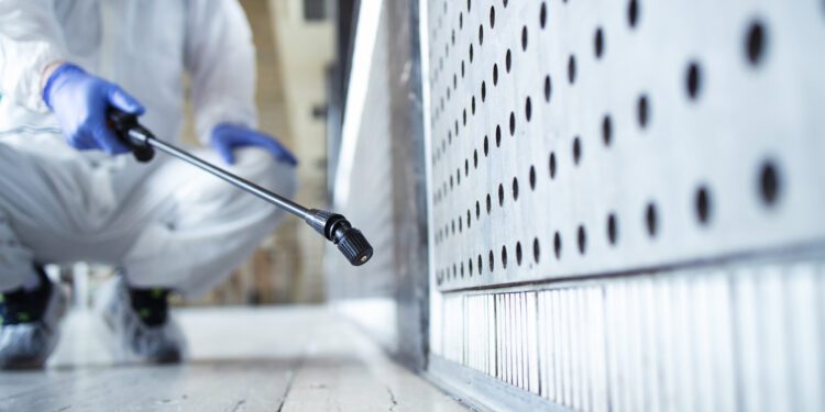 Unrecognizable person in white chemical protection suit doing disinfection of public areas to stop spreading highly contagious corona virus.