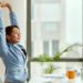 Young smiling businesswoman stretching with her eyes closed while working on a computer in the office.